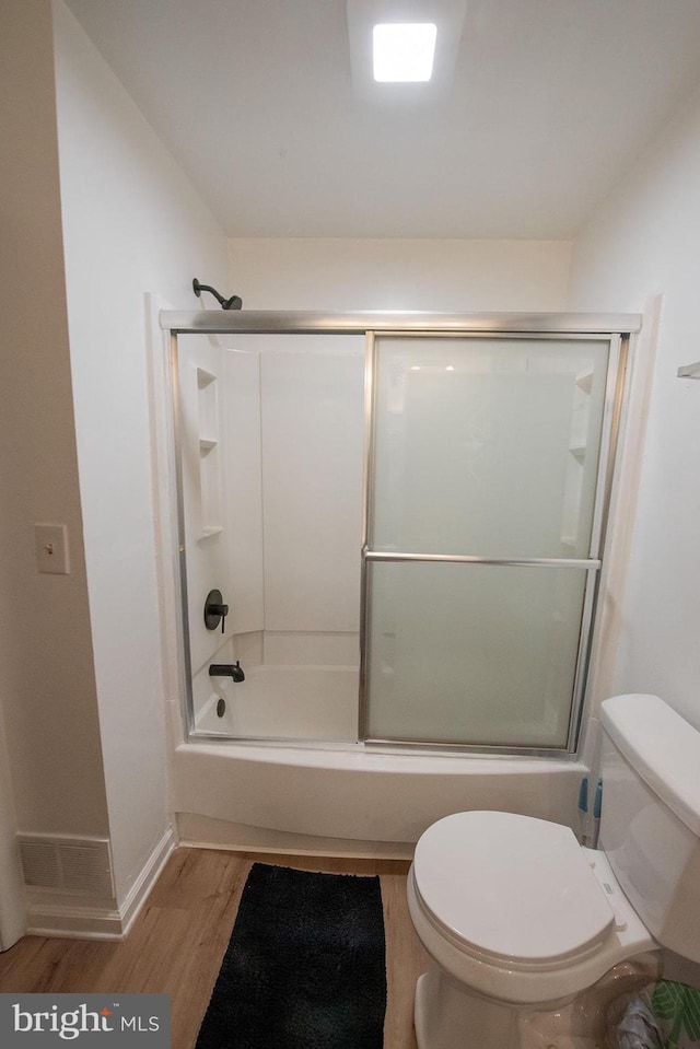 bathroom with toilet, wood finished floors, shower / bath combination with glass door, and baseboards