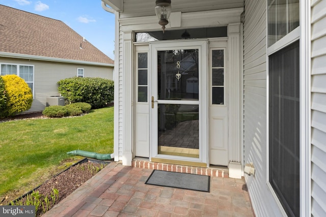 view of exterior entry featuring central air condition unit and a lawn
