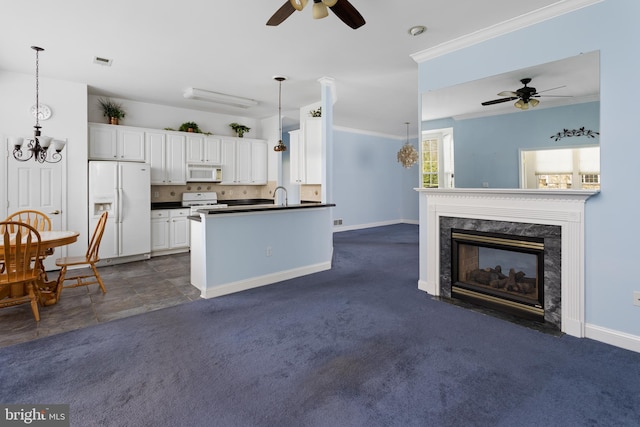 kitchen with a sink, dark countertops, white appliances, ceiling fan with notable chandelier, and a premium fireplace