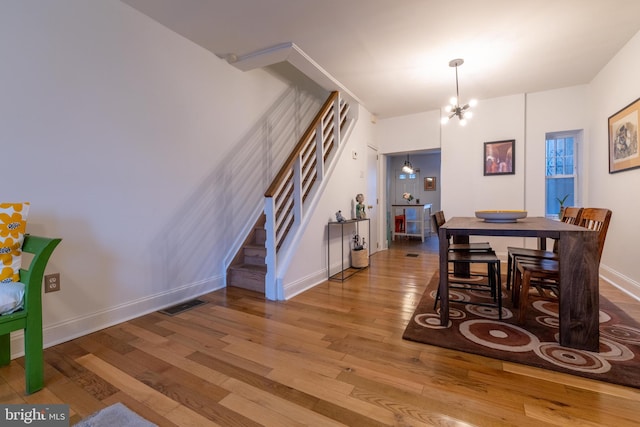 dining area with baseboards, an inviting chandelier, stairway, visible vents, and hardwood / wood-style floors