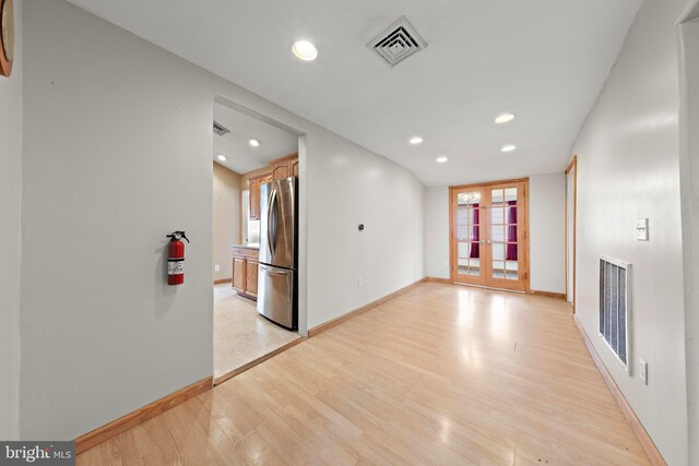 unfurnished living room with light wood finished floors, visible vents, baseboards, and french doors