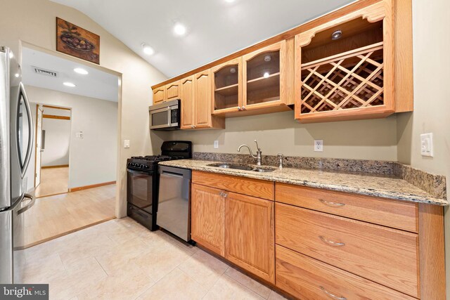 kitchen with glass insert cabinets, appliances with stainless steel finishes, light stone counters, a sink, and lofted ceiling