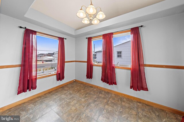 empty room with baseboards, a raised ceiling, an inviting chandelier, and stone finish flooring