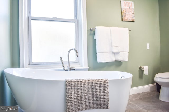 bathroom featuring toilet, baseboards, a freestanding tub, and a healthy amount of sunlight
