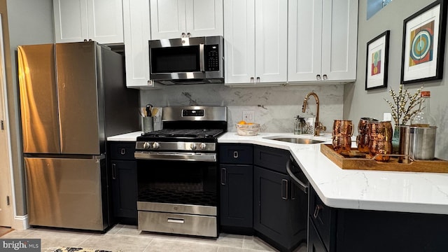 kitchen featuring light tile patterned floors, white cabinetry, light stone countertops, appliances with stainless steel finishes, and a sink