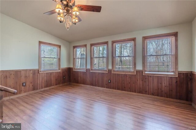 empty room with a ceiling fan, wooden walls, wainscoting, wood finished floors, and lofted ceiling