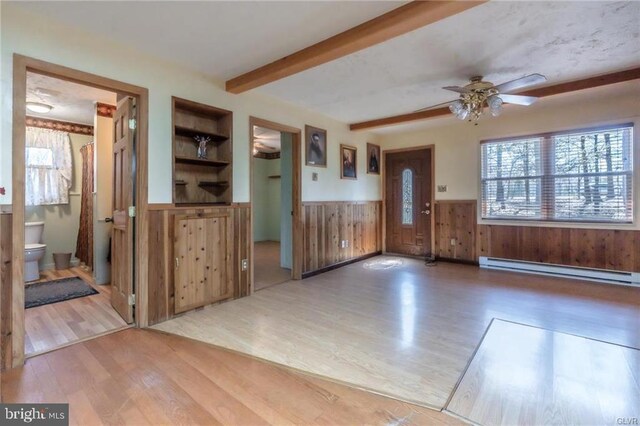 interior space with baseboard heating, a wainscoted wall, beam ceiling, ceiling fan, and wood finished floors
