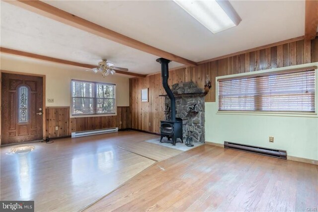 unfurnished living room with wood walls, a wood stove, a baseboard radiator, and beam ceiling