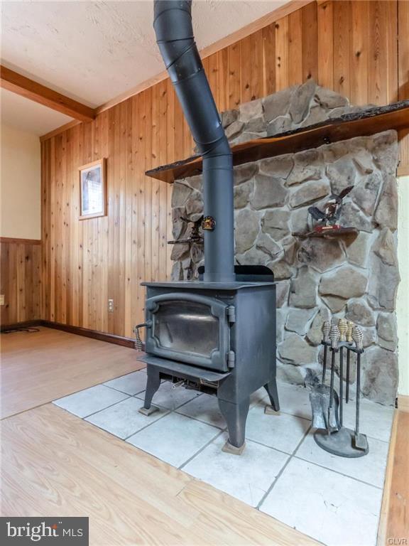room details featuring wood walls, wood finished floors, a wood stove, and beamed ceiling