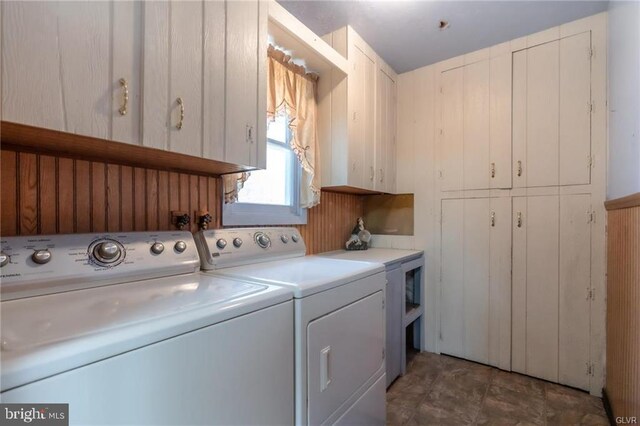 clothes washing area with cabinet space, wood walls, and washing machine and dryer