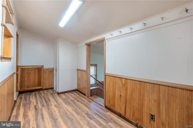 empty room featuring light wood-style floors, lofted ceiling, and a wainscoted wall