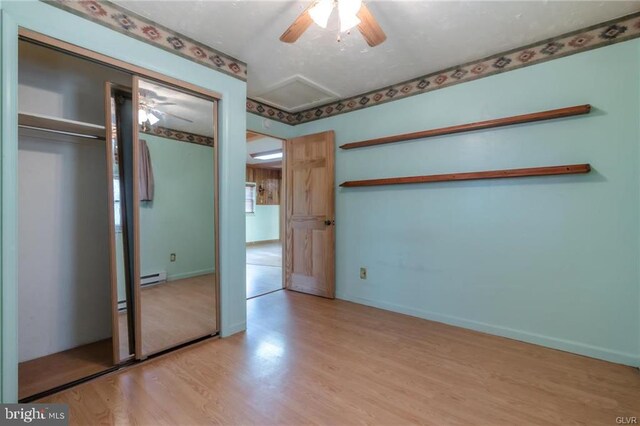 unfurnished bedroom featuring a closet, baseboards, baseboard heating, attic access, and wood finished floors