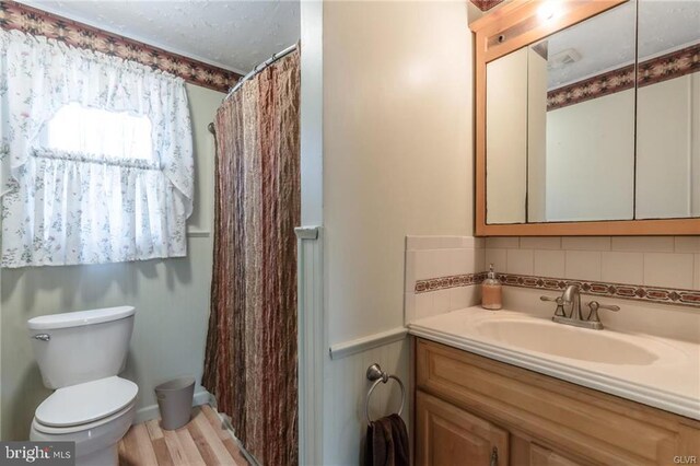 full bath featuring a shower with shower curtain, toilet, vanity, wood finished floors, and backsplash