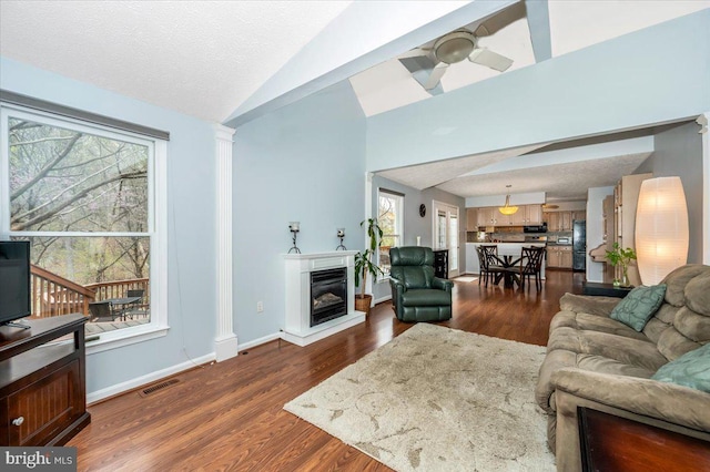 living area with a ceiling fan, dark wood-style floors, a glass covered fireplace, and lofted ceiling