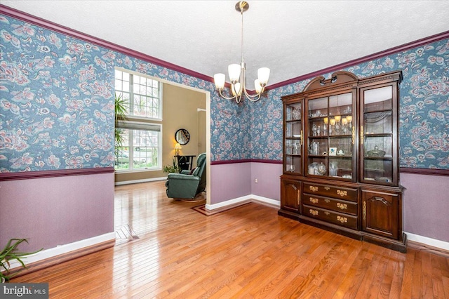 dining area featuring wood-type flooring, a wainscoted wall, a notable chandelier, and wallpapered walls
