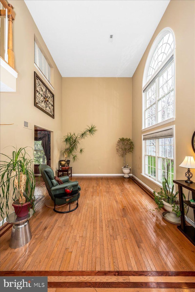 sitting room with hardwood / wood-style floors, visible vents, a towering ceiling, and baseboards