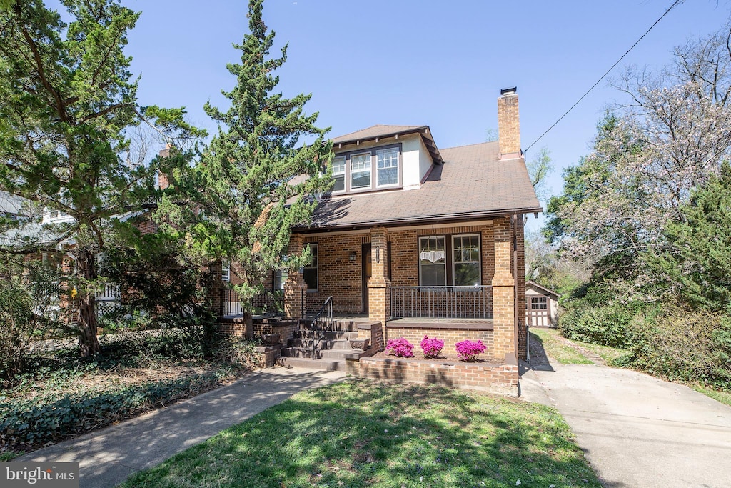 view of front of house featuring brick siding, a porch, a front lawn, and a chimney