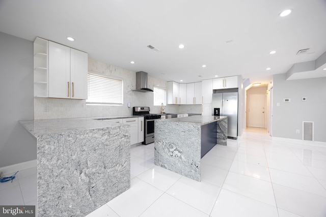 kitchen featuring stainless steel appliances, wall chimney range hood, open shelves, light stone counters, and white cabinetry