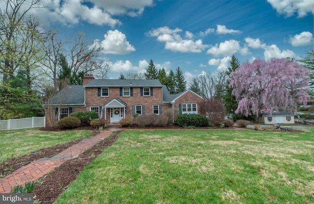 colonial inspired home featuring fence, a chimney, brick siding, and a front yard