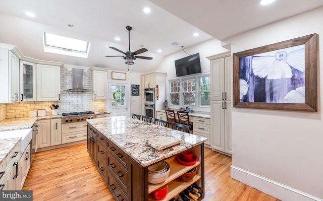 kitchen with wall chimney range hood, open shelves, stainless steel appliances, light wood finished floors, and backsplash
