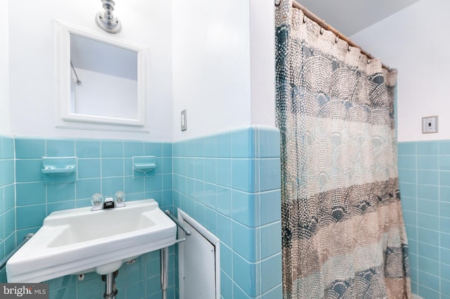 full bathroom featuring a shower with curtain, a wainscoted wall, a sink, and tile walls