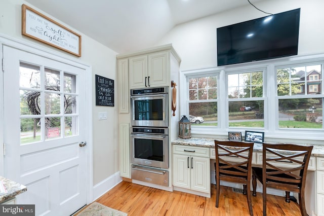 kitchen with a warming drawer, light wood-style floors, lofted ceiling, light stone counters, and double oven