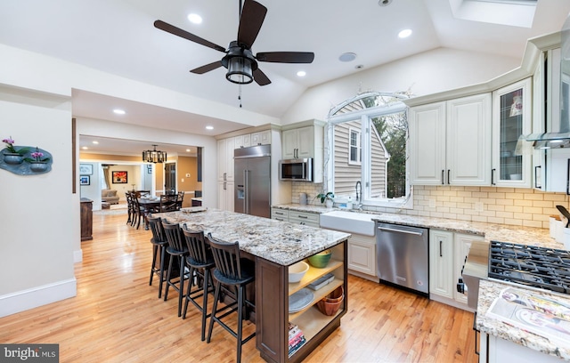 kitchen featuring lofted ceiling, stainless steel appliances, a sink, a kitchen island, and light wood-style flooring