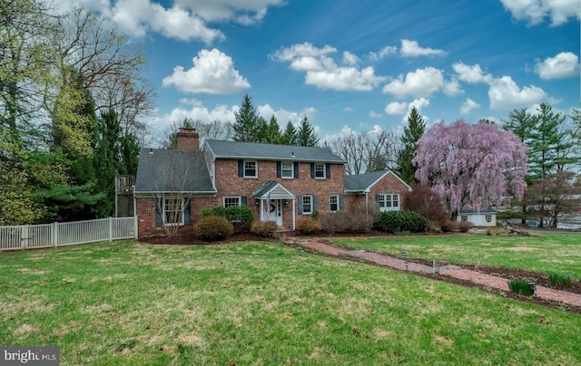 colonial-style house featuring brick siding, fence, a chimney, and a front yard