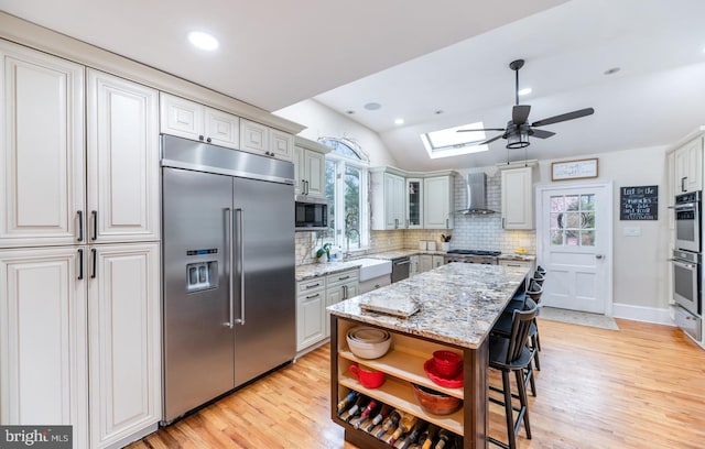 kitchen with wall chimney range hood, a healthy amount of sunlight, stainless steel appliances, and a sink