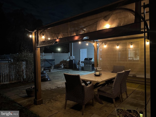 patio at night with a fenced backyard, outdoor dining area, and a grill
