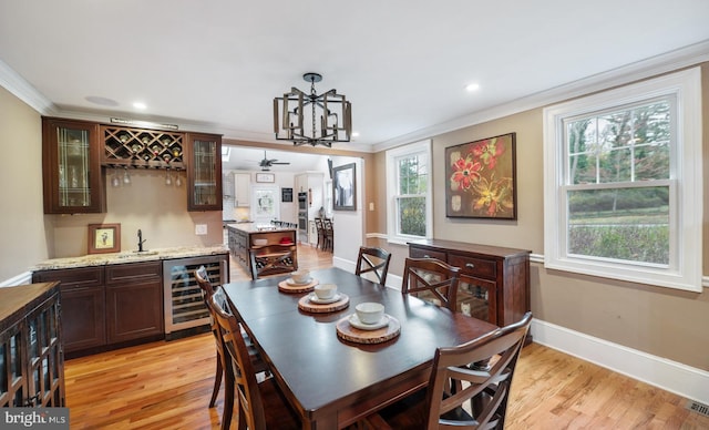 dining space featuring light wood finished floors, crown molding, indoor wet bar, and wine cooler