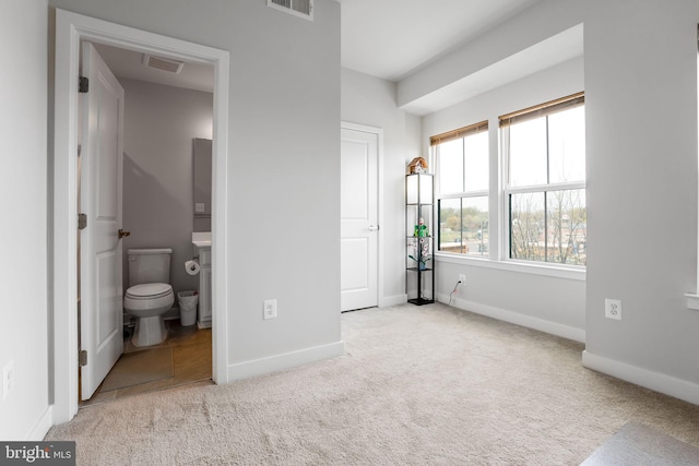 unfurnished bedroom with carpet floors, baseboards, ensuite bath, and visible vents
