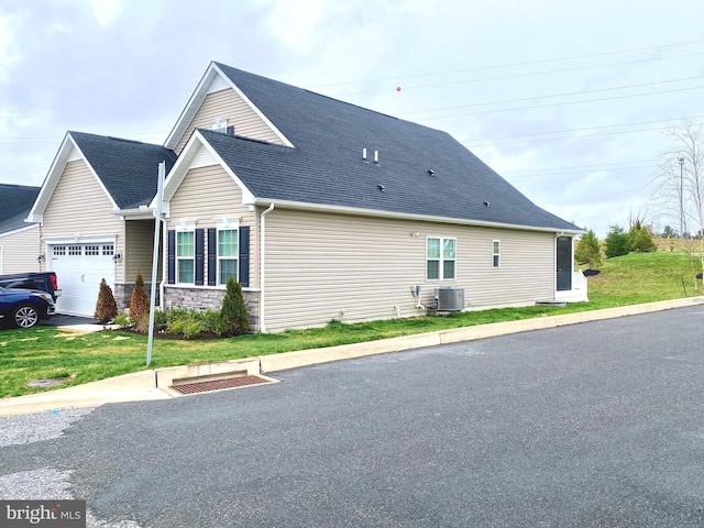 view of side of home featuring a yard, stone siding, a garage, central air condition unit, and roof with shingles