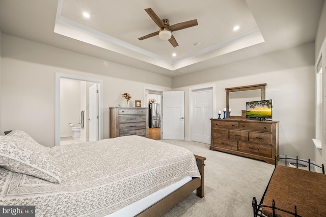 bedroom with a raised ceiling, connected bathroom, recessed lighting, and light carpet