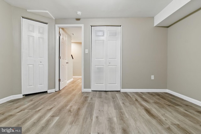 unfurnished bedroom with multiple closets, light wood-type flooring, and baseboards