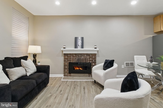 living area featuring light wood finished floors, recessed lighting, baseboards, and a brick fireplace
