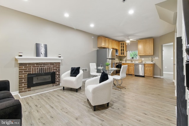 living room featuring baseboards, light wood-type flooring, ceiling fan, a fireplace, and recessed lighting