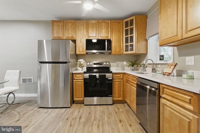 kitchen with stainless steel appliances, a sink, light wood-style flooring, and light countertops