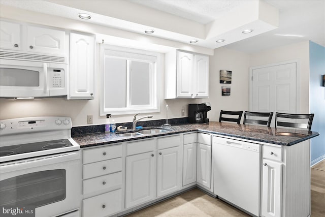 5401 Coastal Hwy Unit 306, Ocean City, MD 21842 - kitchen with dark stone counters, white appliances, a peninsula, white cabinetry, and a sink