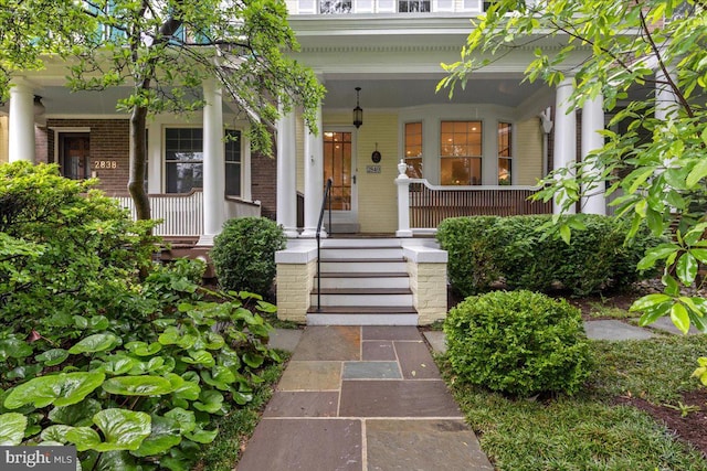 doorway to property featuring a porch and brick siding