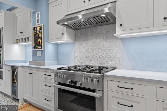 kitchen featuring appliances with stainless steel finishes, under cabinet range hood, wine cooler, and light countertops