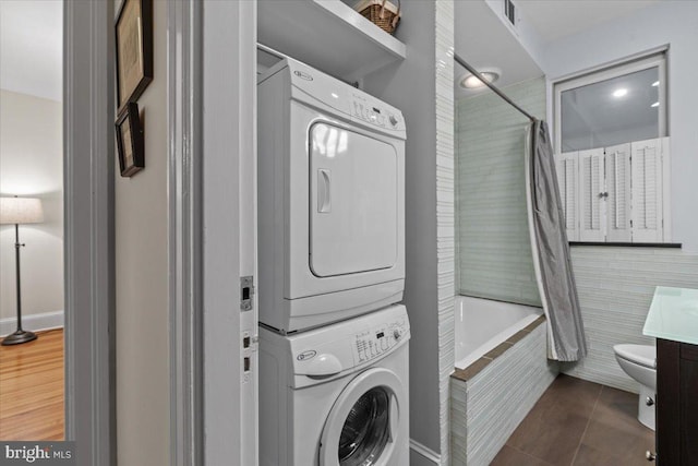 clothes washing area with stacked washing machine and dryer and tile patterned floors