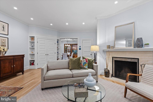living area featuring light wood-type flooring, a chandelier, a fireplace with flush hearth, crown molding, and recessed lighting