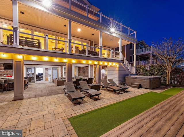 back of house at night with a patio, a hot tub, and a balcony