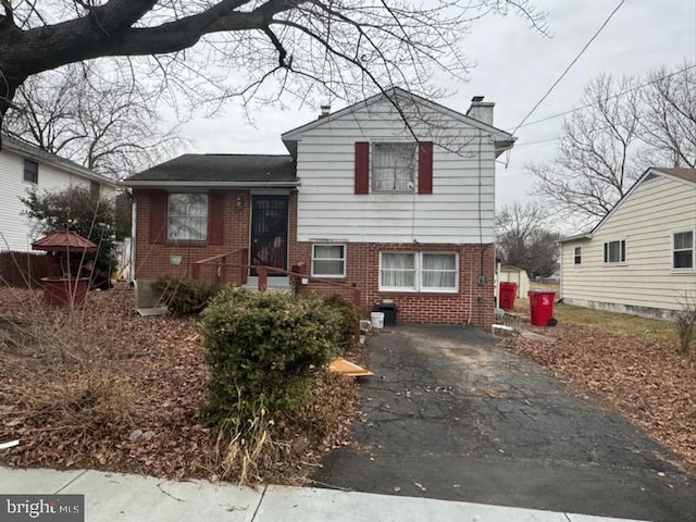 split level home featuring aphalt driveway, brick siding, and a chimney