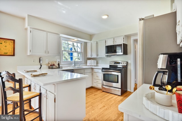 kitchen featuring a sink, white cabinetry, light countertops, a peninsula, and appliances with stainless steel finishes