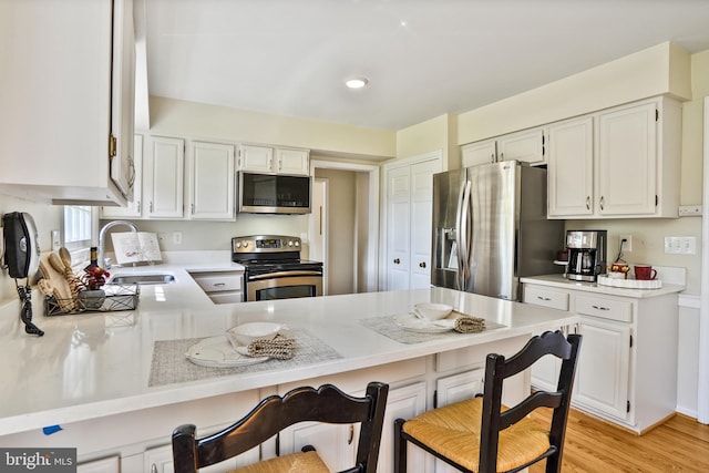 kitchen featuring a peninsula, a sink, a kitchen bar, light countertops, and appliances with stainless steel finishes