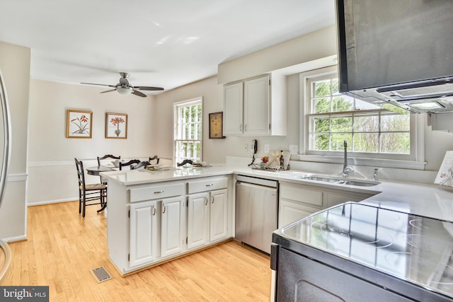 kitchen with a peninsula, stainless steel dishwasher, a sink, visible vents, and white cabinetry