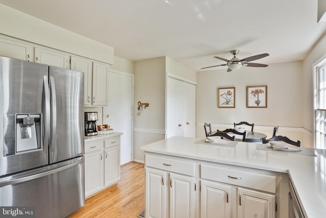 kitchen featuring light wood finished floors, light countertops, a ceiling fan, stainless steel fridge, and white cabinetry