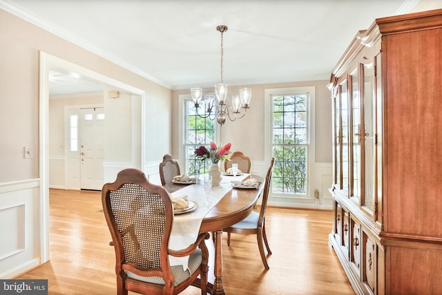dining space with a wainscoted wall, an inviting chandelier, light wood-style floors, a decorative wall, and ornamental molding